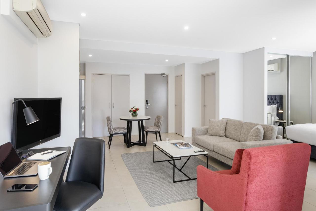 Meriton Suites Kent Street, Σίδνεϊ Εξωτερικό φωτογραφία The photo shows a modern living space that includes a comfortable seating area and a small dining table. There is a light-colored sofa accompanied by a red armchair, creating a cozy atmosphere. A black desk with a computer is positioned nearby, along