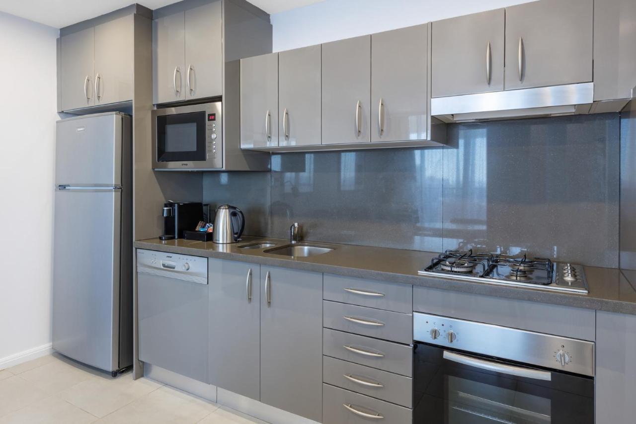 Meriton Suites Kent Street, Σίδνεϊ Εξωτερικό φωτογραφία The photo shows a modern kitchen with a sleek design. It features gray cabinetry with multiple drawers and cabinets, a stainless steel oven, a gas cooktop, and a microwave above it. There's also a stainless steel refrigerator on the left, and a kettl