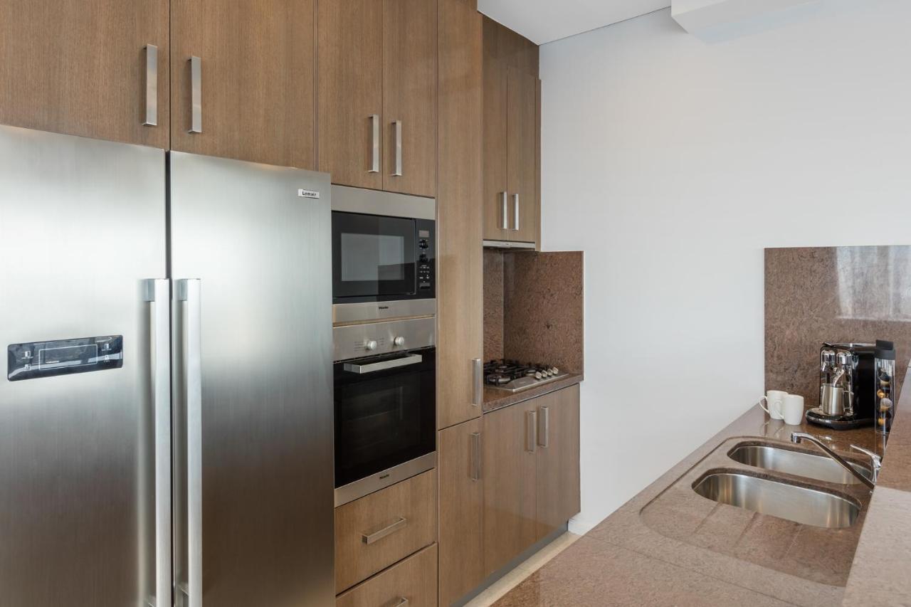 Meriton Suites Kent Street, Σίδνεϊ Εξωτερικό φωτογραφία The photo shows a modern kitchen featuring a combination of appliances and cabinetry. On the left, there is a stainless steel refrigerator. Next to it, built into the cabinetry, is an oven and a microwave. The countertop is smooth and made of a light