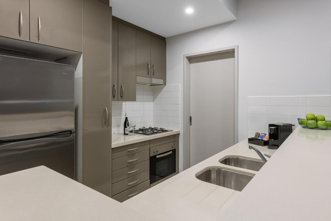 Meriton Suites Kent Street, Σίδνεϊ Εξωτερικό φωτογραφία The photo shows a modern kitchen featuring sleek cabinetry in a neutral tone. There is a stainless steel refrigerator on the left and a built-in oven and stovetop in the middle. The countertop is light-colored and includes a double sink. On the right
